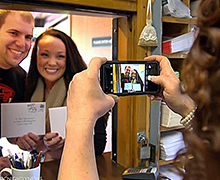Bridal Veil, OR, Retail Associate Tara Stiller snaps a photo of Christine Dougherty and Tyler Kennedy mailing their wedding invitations.