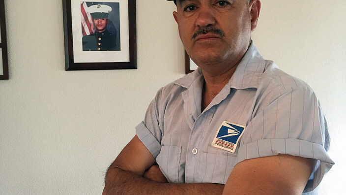 Cheyenne, WY, Letter Carrier Stephan Martinez stands near a photo of himself in his Marine uniform.