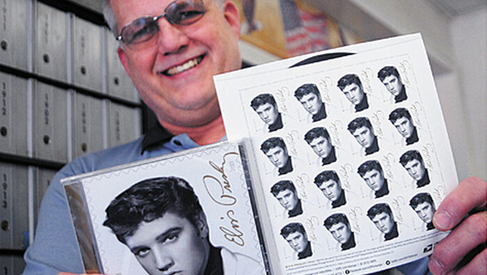 Employee shows a sheet of Music Icons: Elvis Presley stamps, along with the “Elvis Presley Forever” CD