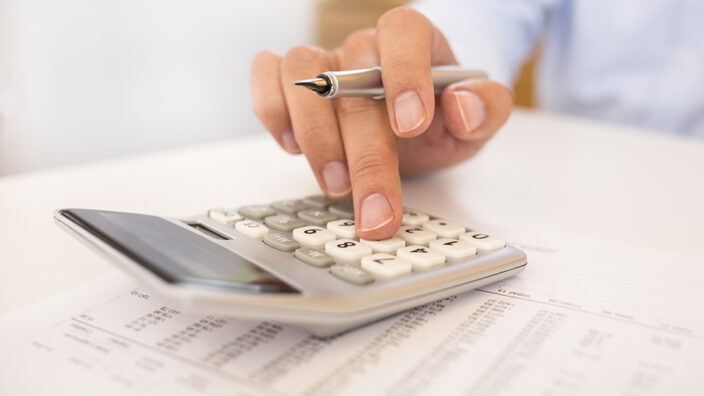 Someone's hand holding a pen and working on a calculator