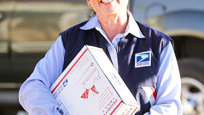 An employee with a Priority Mail package and a Mobile Delivery Device.