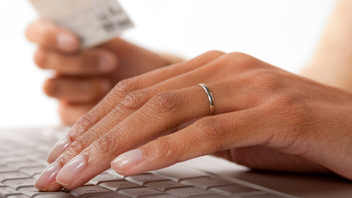 Someone's hands using a computer and holding a credit card.