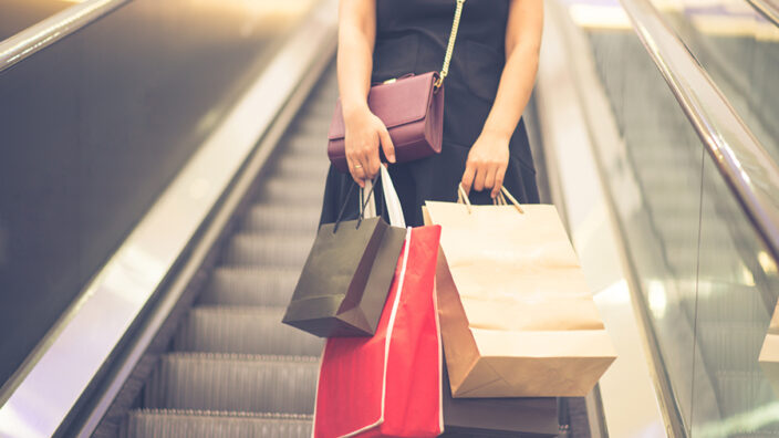 Someone on a escalator holding shopping bags.