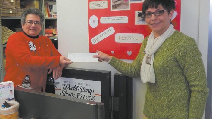 Wysox Postmaster Penny Horton hands a letter to Letter Carrier Kathy Camp.