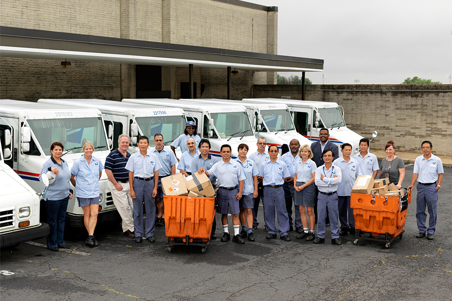 Several postal employees with some hampers standing in front of some LLVs.