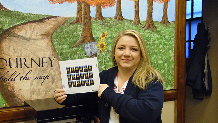 Iron, MN, Retail Associate Denise Jensen holds a Medal of Honor: Vietnam War stamp sheet.