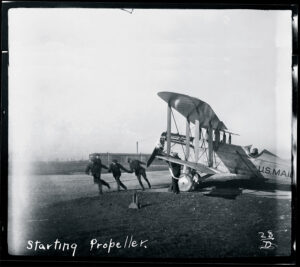 A plane’s engine is cranked in the early 1920s.