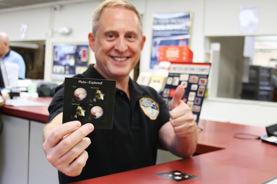 Alan Stern, principal investigator of the New Horizons mission to Pluto, shows off his Pluto — Explored! stamp purchase at the Boulder, CO, Post Office.