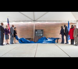 The memorial is unveiled by, from left, Curseen-Morris Processing and Distribution Center Plant Manager Darrell Young, Malone, Lee Jackson and his wife Joan, APWU Local 140 President Dena Briscoe, NPMHU Local 305 Branch President Calvin Vines, and retired postal leaders Theresa Gibbs and Tim Haney. Vacca, who isn’t shown, also participated in the unveiling.