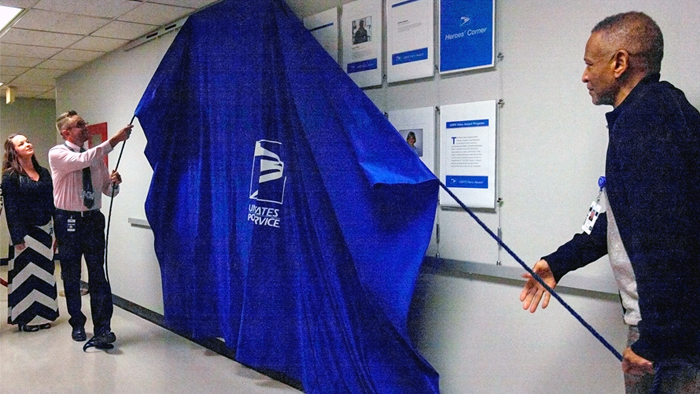 Daniel Toney, left, his wife Jessica and Derrick Coleman unveil a display honoring postal heroes at USPS headquarters this year.