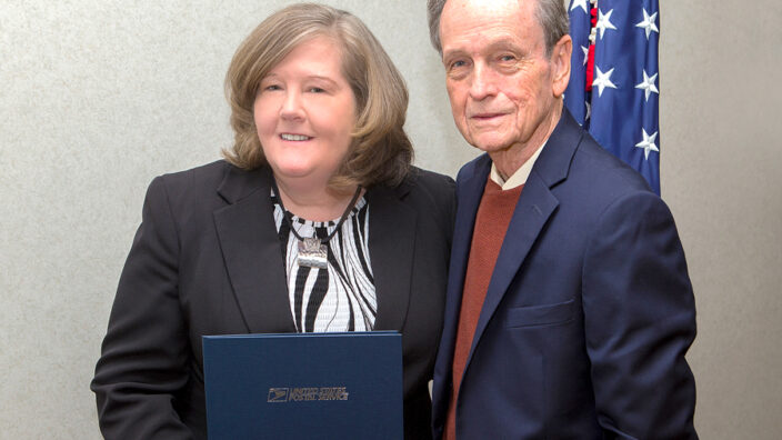 PMG Megan J. Brennan receives her 30-year pin from James H. Bilbray, chairman of the USPS Board of Governors.