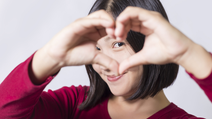 Asian woman wearing red holds up hands in shape of heart