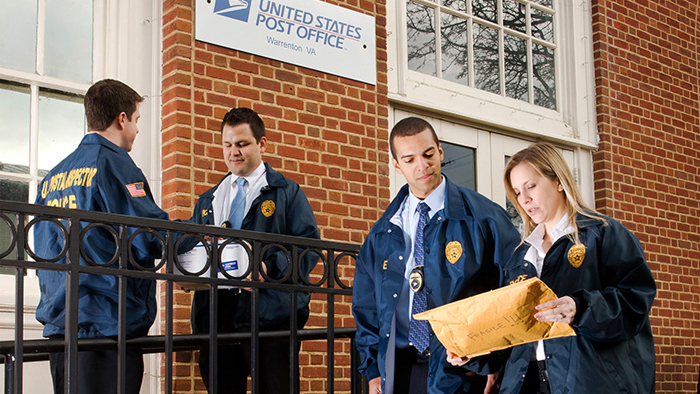 Four Postal Inspectors work in front of a Post Office