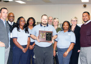 Gathering to display the Vidalia, GA, Post Office’s plaque are, from left, Postmaster J.T. Warnock, Sumlar, Tina Bentley, Velma Wadley, Caleb Harrison, Martin, Julie Register, Kim Bacon, Sigmon and Manager of Post Office Operations Michael Crawley.