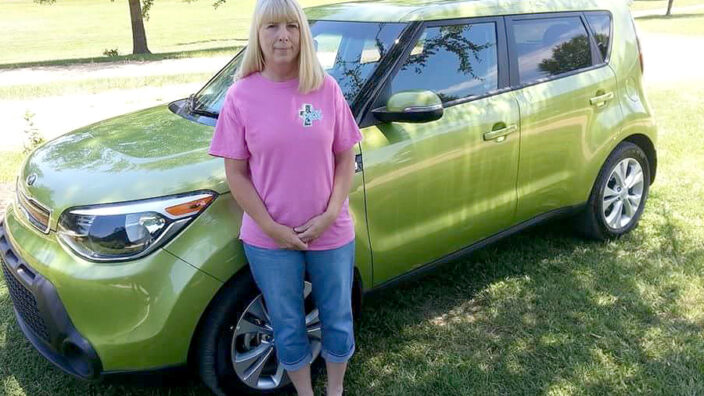 Woman stands in front of green car
