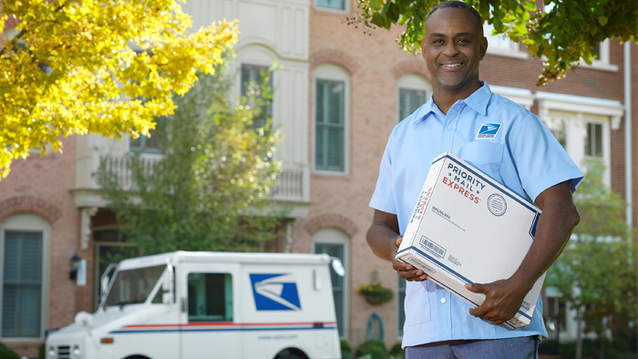 Male mail carrier holds package infront of vehicle