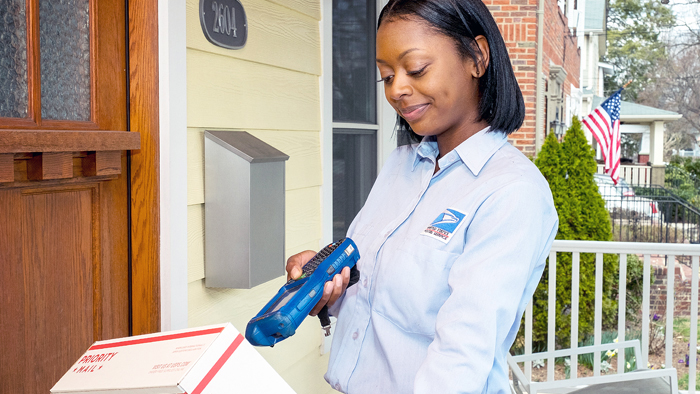 Female mail carrier scans package outside home