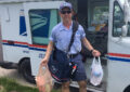 Male carrier holds bagged donations in front of mail truck