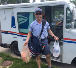 Male carrier holds bagged donations in front of mail truck