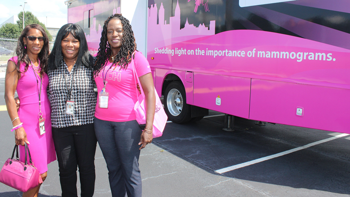 Three women stand next to pink bus