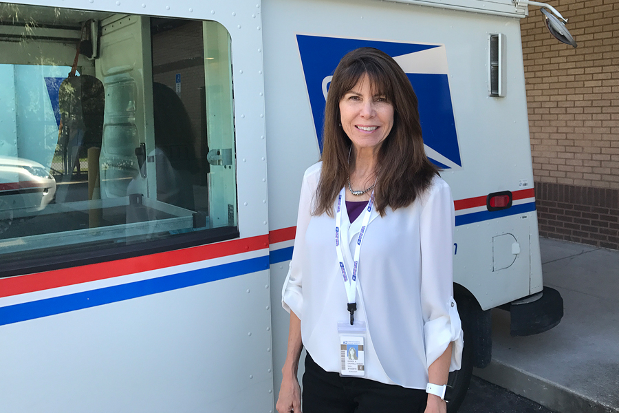 Woman in shirt stands in front of postal truck