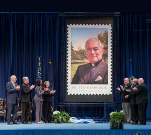 People stand near Father Theodore Hesburgh stamp display