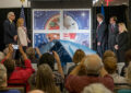 People on stage watch drape fall from stamp artwork