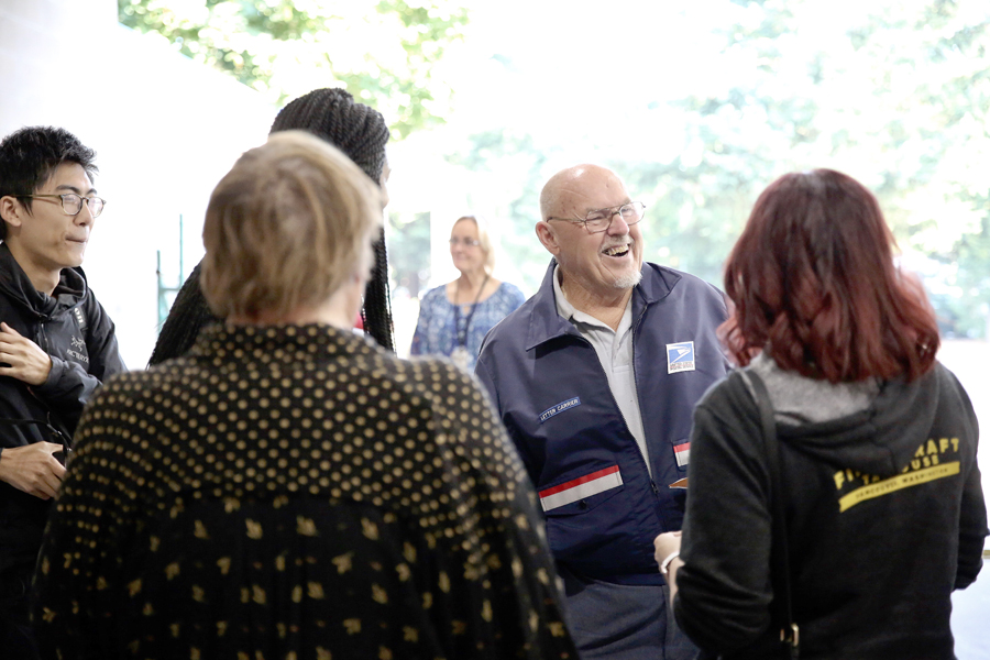 Bald man with glasses laughs surrounded by people