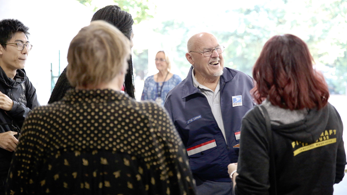 Bald man in glasses laughs surrounded by people