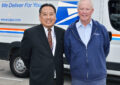 Man in suit stands next to man in postal uniform