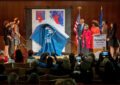 People stand on stage as drape covering stamp artwork falls