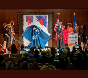 People stand on stage as drape covering stamp artwork falls