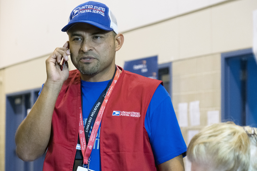 Man talk on phone in blue postal hat and red vest