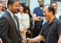 Two men shake hands and smile as others watch