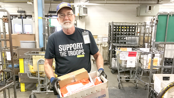 Vet holding mail tray wearing 'Support Our Troops' shirt