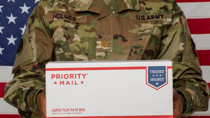 Person wearing Army uniform holding Priority Mail box