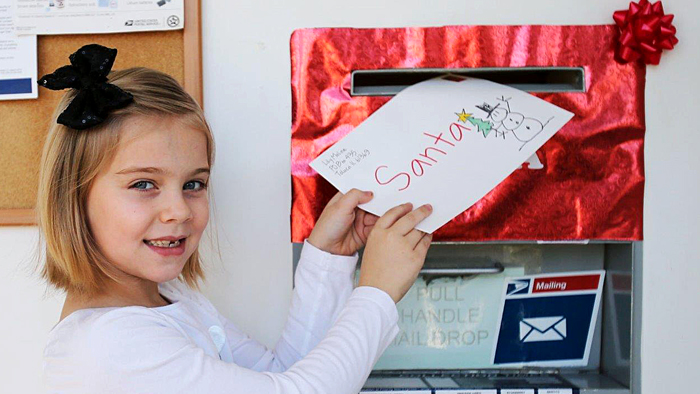 Little girl holds letter toward mailbox