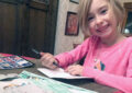 Child sits at table addressing envelopes