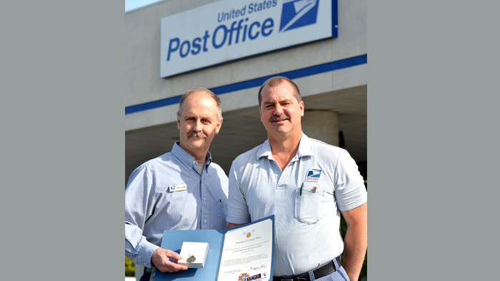Two employees hold award outside Post Office