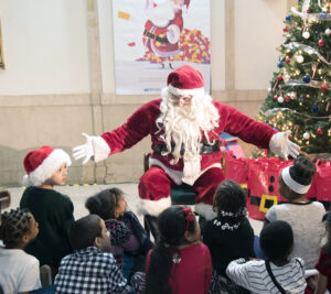 Santa Claus spreads his arms wide as he speaks to children