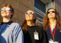 Three women wearing special glasses gaze upward