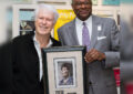 Two men hold framed stamp artwork