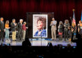 People stand on stage as stamp artwork is unveiled