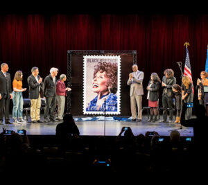 People stand on stage as stamp artwork is unveiled