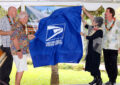 People pull drape of stamp artwork on stage