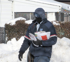 Letter carrier in heavy winter gear walks through snowy neighborhood