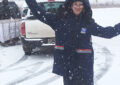 Letter carrier gestures enthusiastically as snow falls