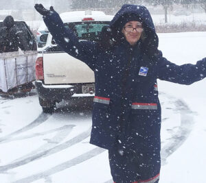 Letter carrier gestures enthusiastically as snow falls