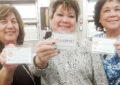 Three women hold tags with charitable causes written on them