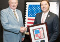 Two men shake hands while holding framed artwork